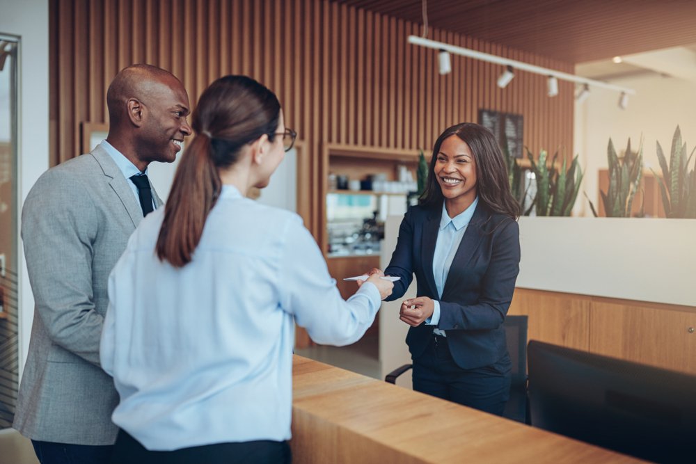 Two,Guests,Giving,Their,Reservation,Details,To,A,Smiling,Concierge